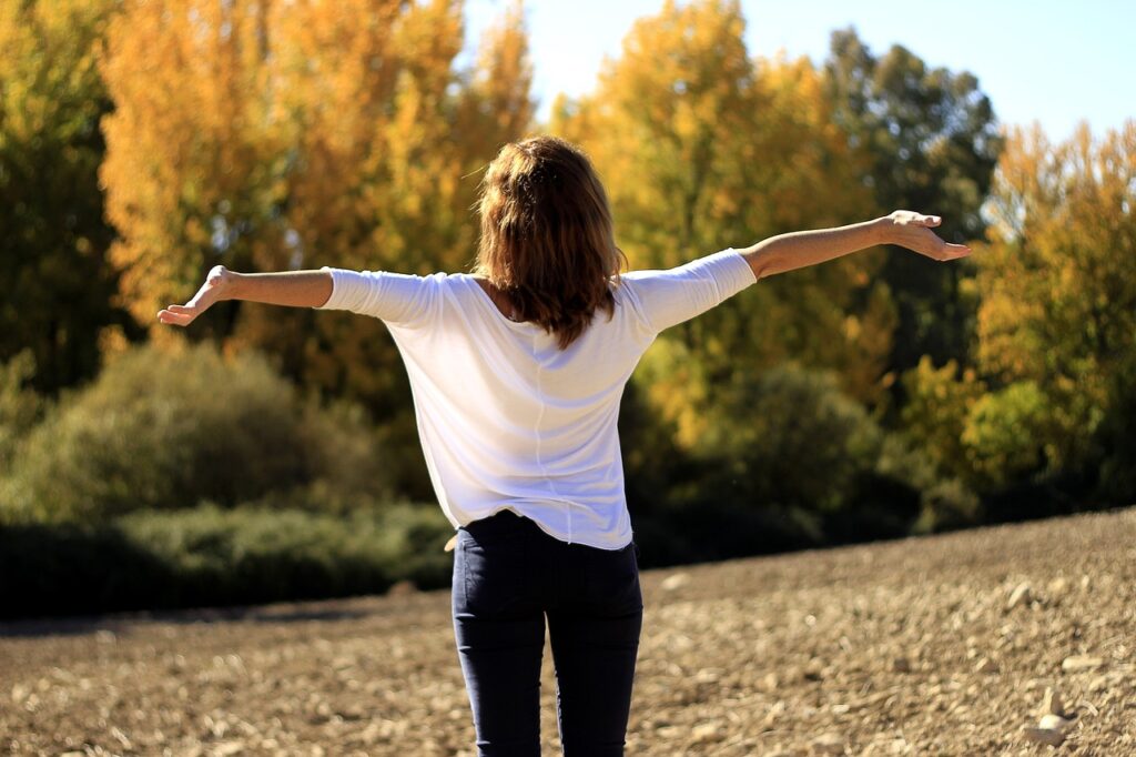 Cohérence cardiaque : une femme respire à l'extérieur, les bras tendus, signe de bien-être et de sérénité