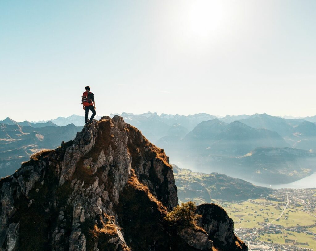 Personne debout au sommet d'une montagne contemplant un vaste paysage naturel, symbolisant la congruence, l'accomplissement personnel, la sérénité et l'harmonie intérieure.