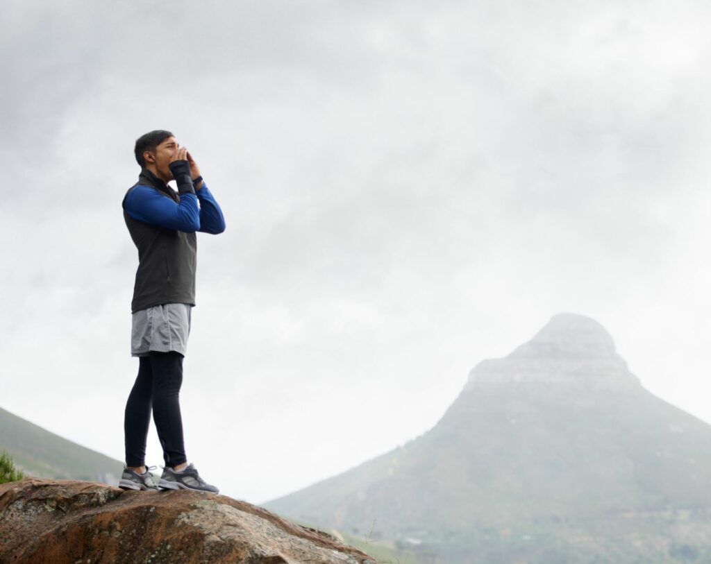 Jeune homme criant dans la montagne et entendant son écho, symbolisant le concept de projeter ses peurs sur les autres comme un reflet de ses insécurités personnelles.