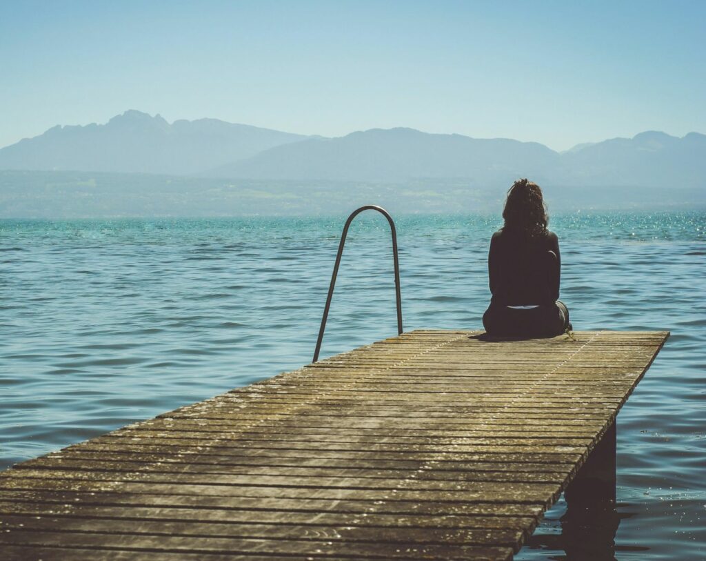 Une femme seule, triste, au bord d'un lac, représentant le désarroi dans lequel les violences psychologiques poussent certaines personnes