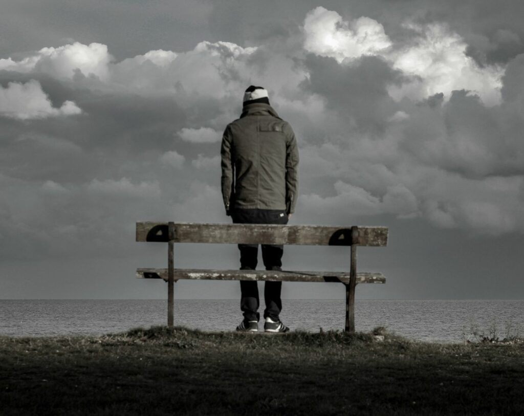 Un homme seul face à la mer, devant un banc, représentant l'isolement lorsque l'on subit des violences psychologiques dans un couple